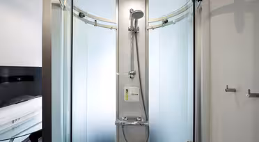 En moderne, buet dusjkabinett i glass med sølvdusjhode og kontrollpanel. Frostete glassdører er delvis åpne, og avslører en elegant design. Baderomsbakgrunnen inkluderer et hvitt og svart fargeskjema.