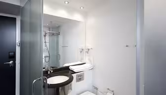 Moderne bad med dusjdør i glass, veggspeil, svart benkevask og hvitt toalett. Håndklær er pent brettet på benken. Designet er elegant med hvite vegger og en minimalistisk stil.